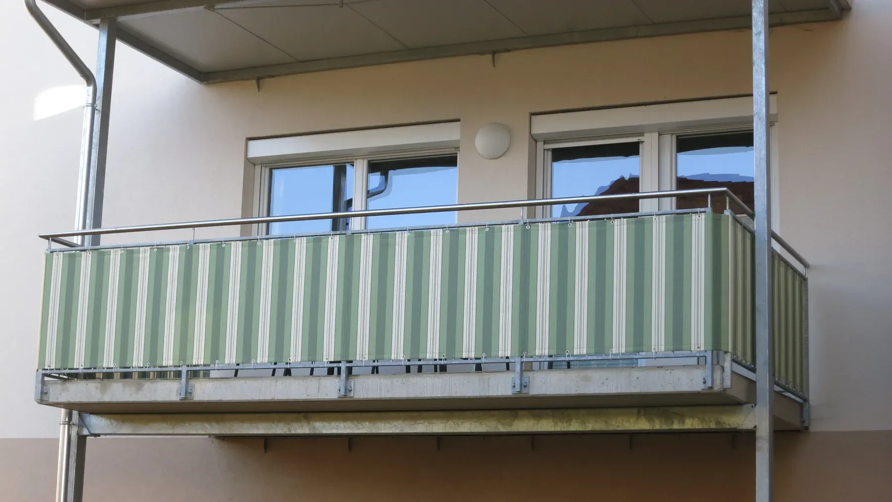 Balkon eines Wohnhauses mit grün-weiß gestreifter Bespannung, die Ösenreihe am Edelstahlgeländer ist gut sichtbar