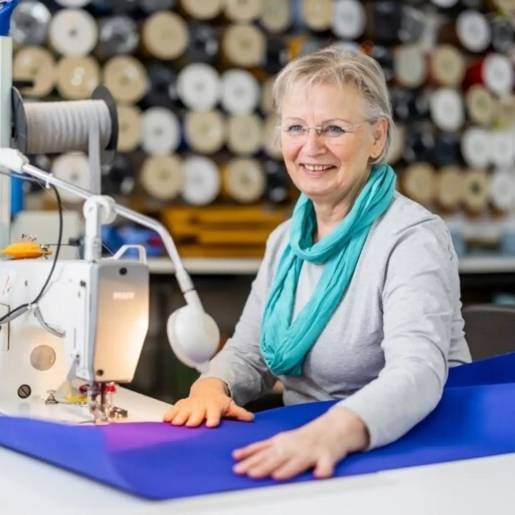 Näherin vernäht ein blaues Acryltuch an der Nähmaschine vor der Garnrollenwand